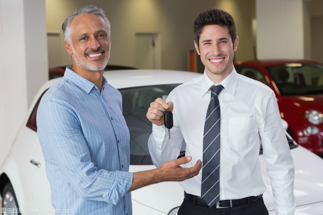 微笑的商人给汽车钥匙给快乐的顾客